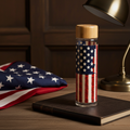 Land of Liberty Glass Water Bottle sitting atop a copy of the Constitution, next to a folded American flag and desk lamp
